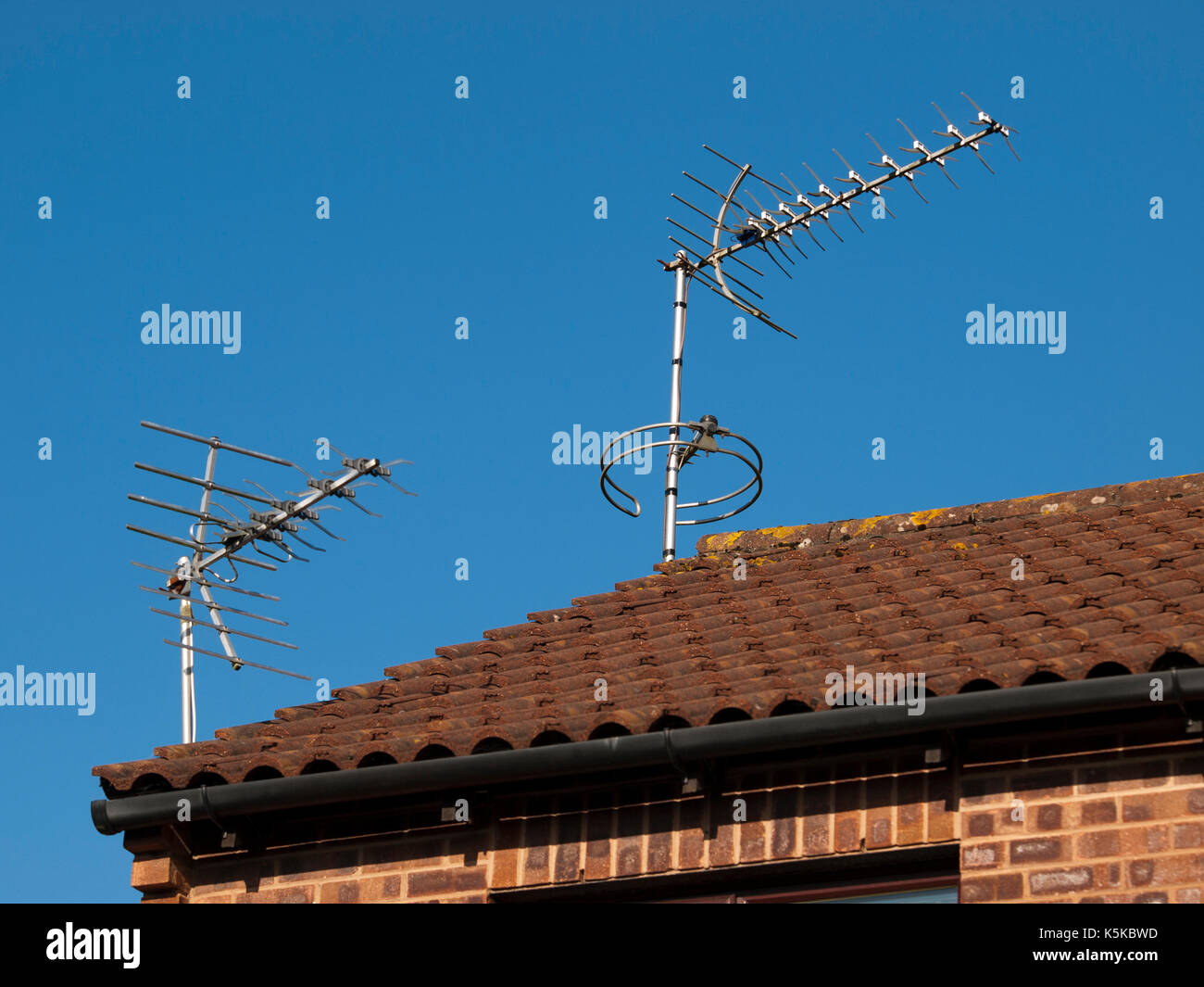 Two TV Aerials on a rooftop set against a clear blue sky Stock Photo