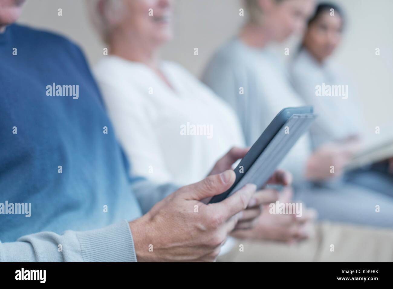 Man using digital tablet with woman in background in waiting room. Stock Photo