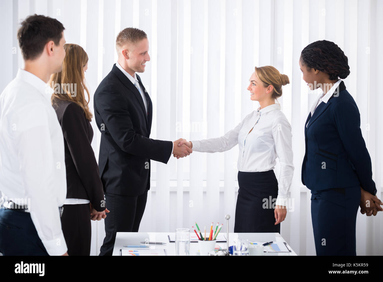 Businesspeople Looking At Two Young Business Partners Shaking Hands In Office Stock Photo