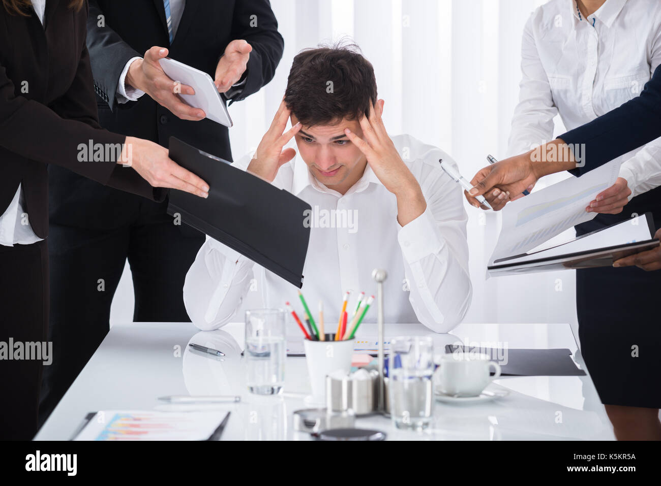 Young Businessman Stressed Out At Work Surrounded By Businesspeople Stock Photo