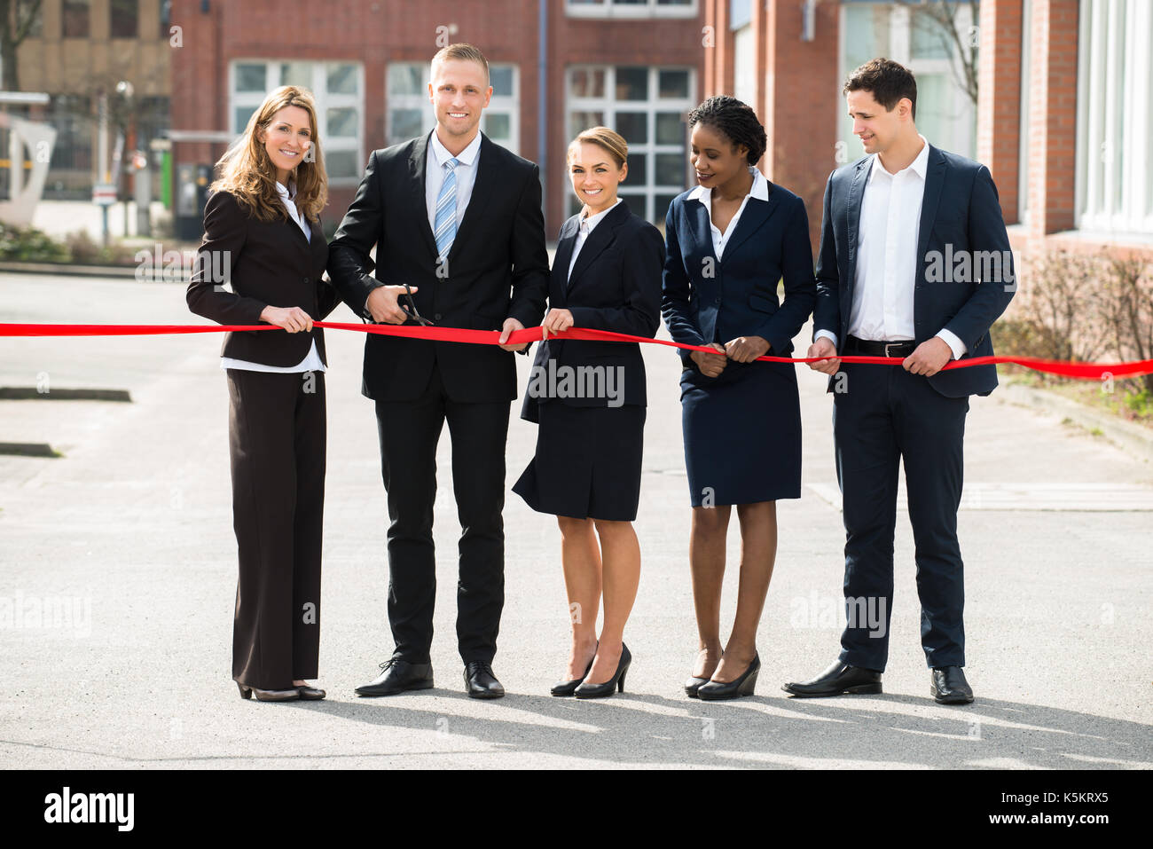 Happy Businesspeople At Opening Cutting Ribbon With Scissor Stock Photo