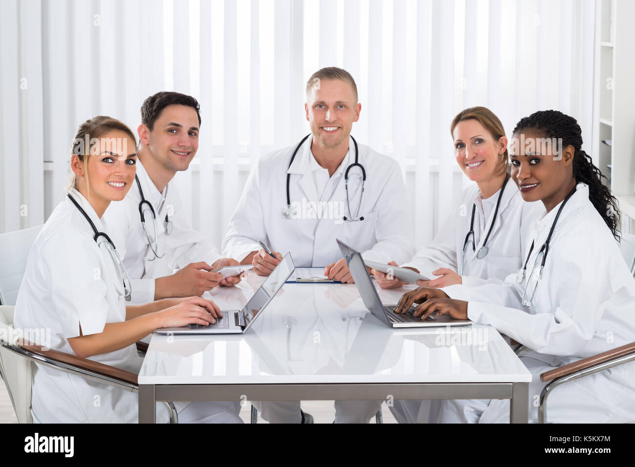 Team Of Happy Doctors Using Digital Tablet And Laptop At The Meeting Stock Photo