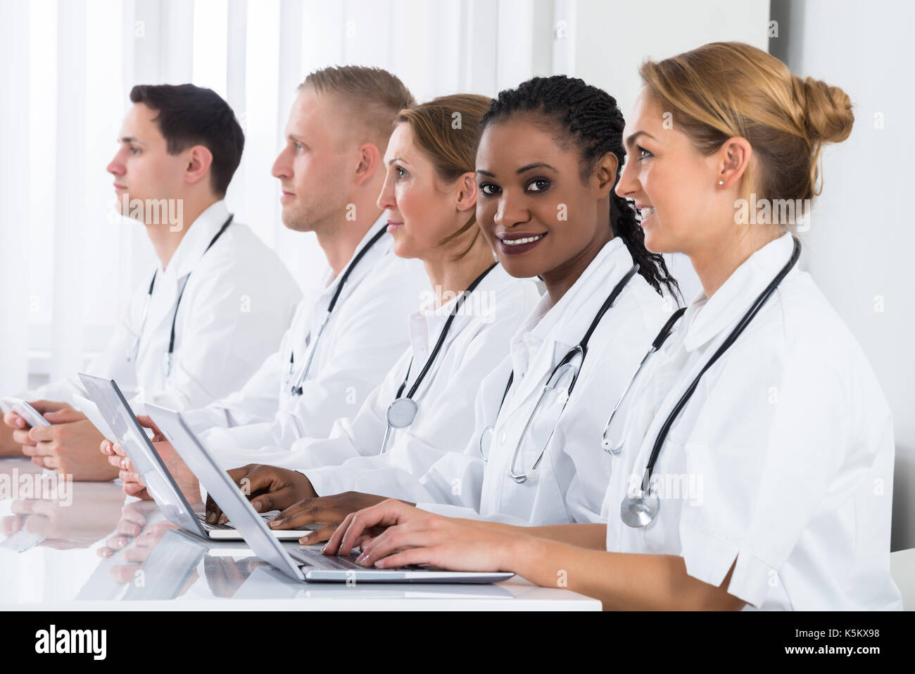 Group Of Doctors In Labcoat Using Laptop At Desk Stock Photo