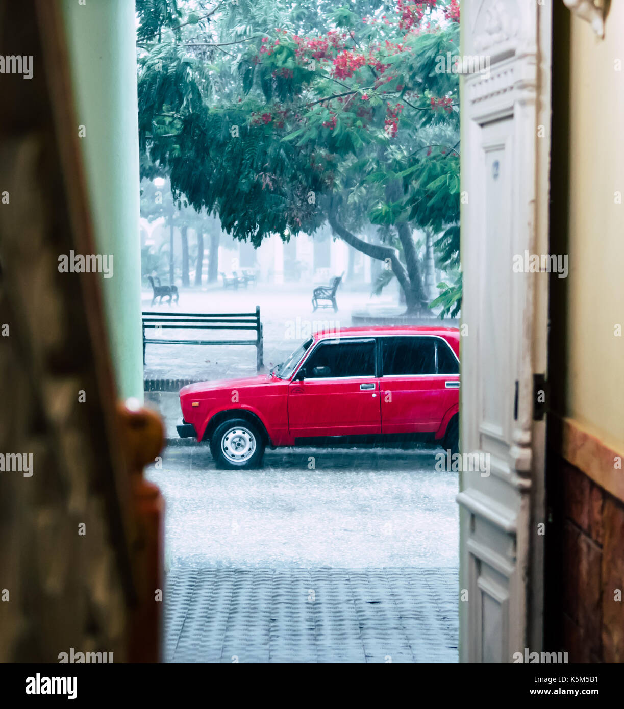 Rainy day in Cuba. Old red car with tinted windows seen parked on