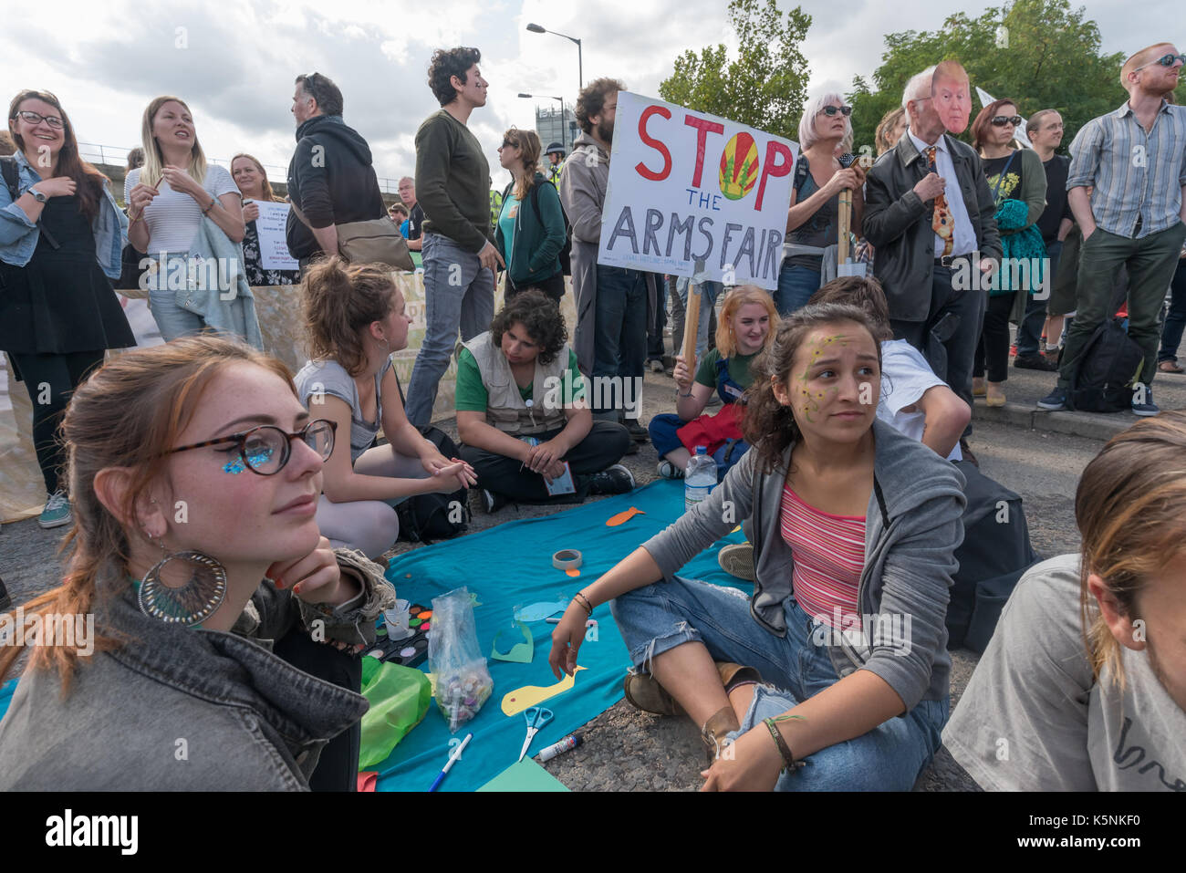 London, UK. 9th Sep, 2017. London, UK. 9th September 2017 Protesters sit on the road at the Festival of Resistance against DSEI Arms Fair to block lorries entering with arms. The Defence & Security Equipment International, backed by the UK government, is where arms companies and arms dealers sell weapons to countries around the world including many repressive regimes. The road at the East Gate was blocked by a lock-on by two protestersand others including this group sat on the road in front of it, with a large group holding a Quaker meeting. Police tried to clear the road and made severa Stock Photo