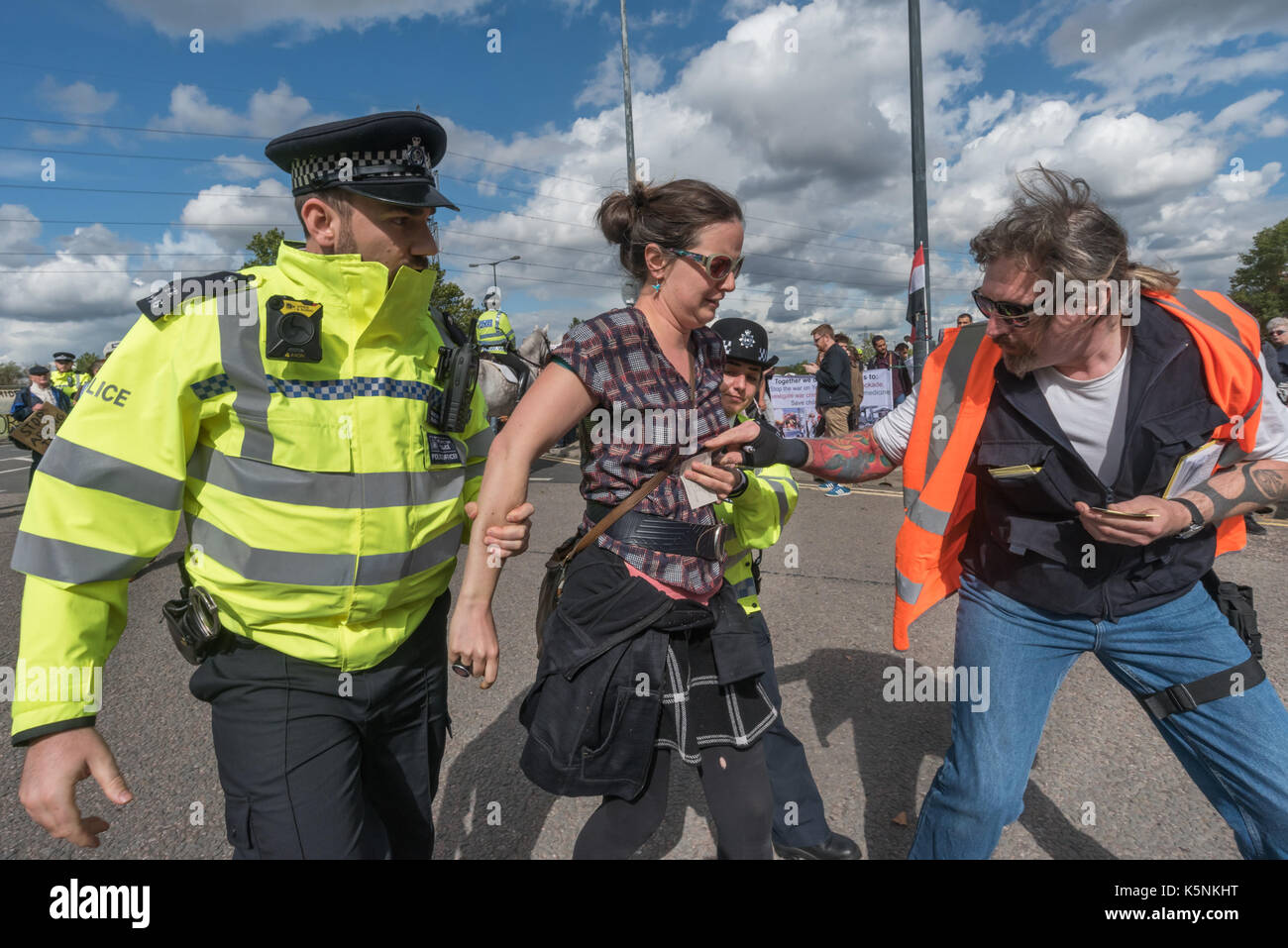 London, UK. 9th Sep, 2017. London, UK. 9th September 2017 Police lead away a woman arrested for sitting on the road at the Festival of Resistance against DSEI Arms Fair to block lorries entering with arms. The Defence & Security Equipment International, backed by the UK government, is where arms companies and arms dealers sell weapons to countries around the world including many repressive regimes. The road at the East Gate was blocked by a lock-on by two protestersand others including this group sat on the road in front of it, with a large group holding a Quaker meeting. Police tried to Stock Photo