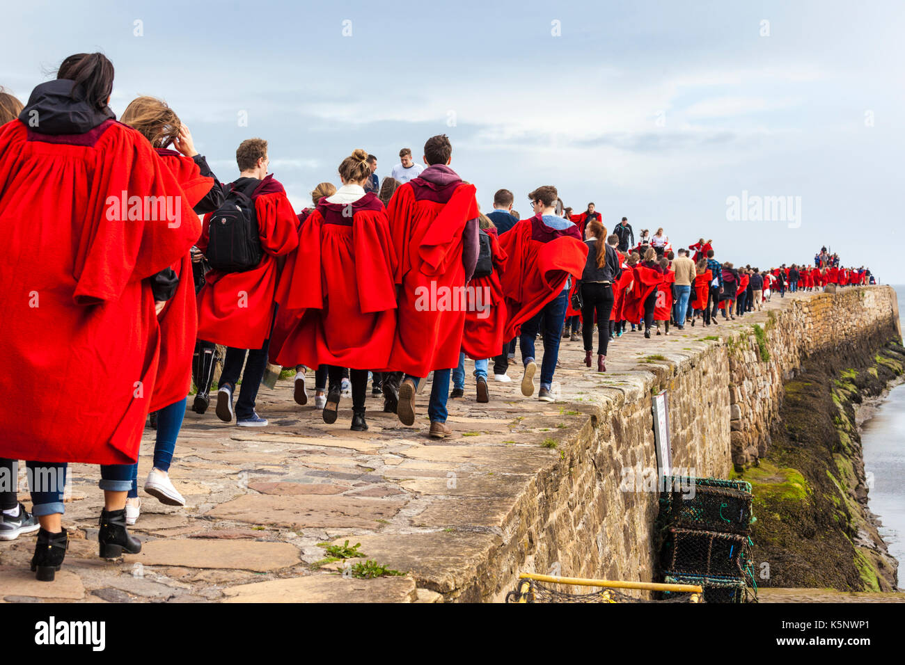 Freshers' Week at St Andrews University, Fife, UK. Students in their red gowns brave the weather to take their traditional Sunday morning walk along the pier. Stock Photo