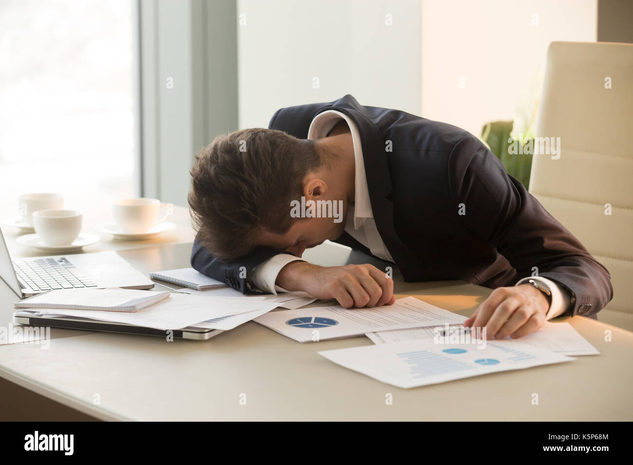Tired young businessman sleeping on desk in office Stock Photo