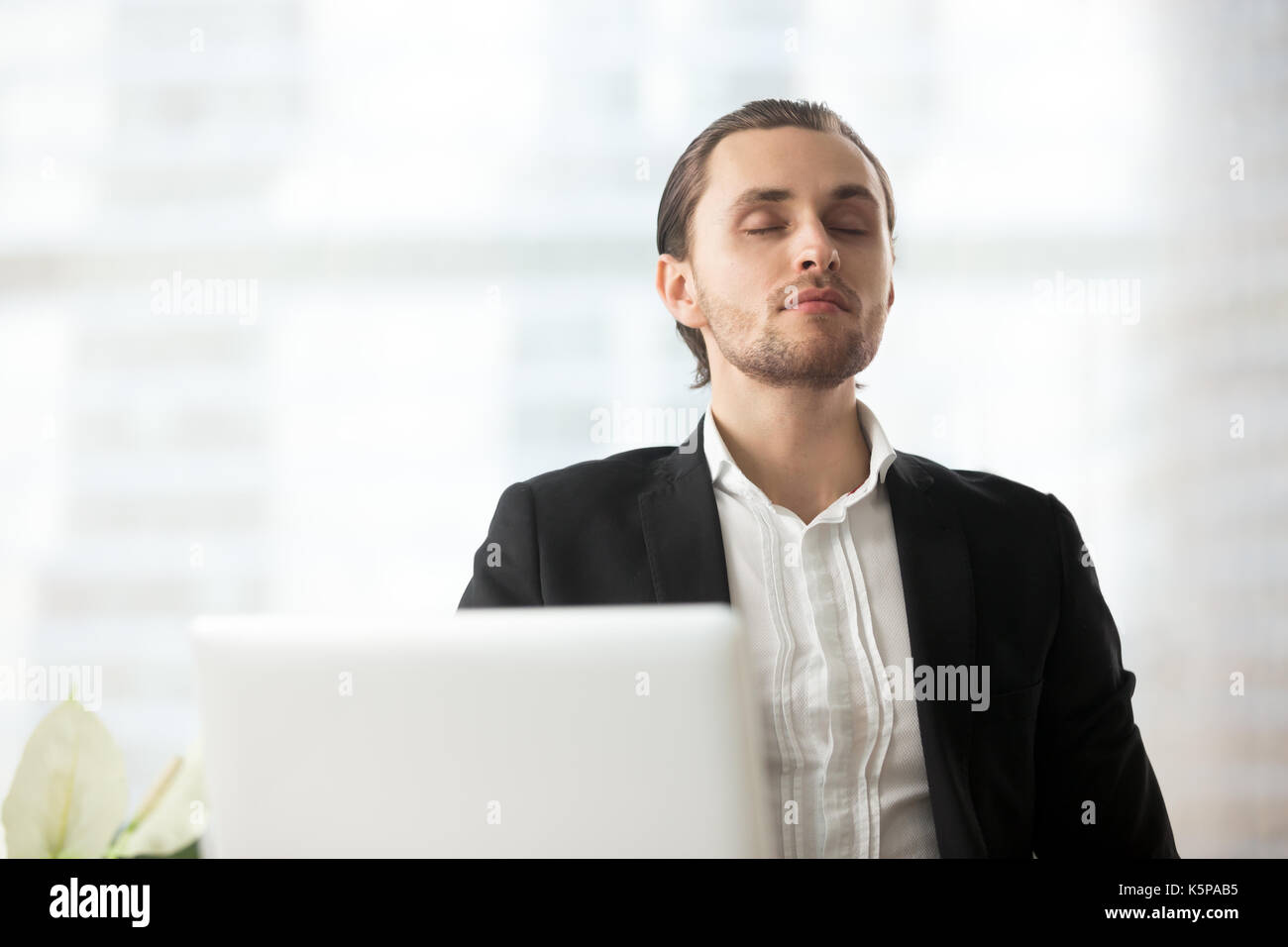 Young calm businessman resting at workplace with eyes closed. Stock Photo