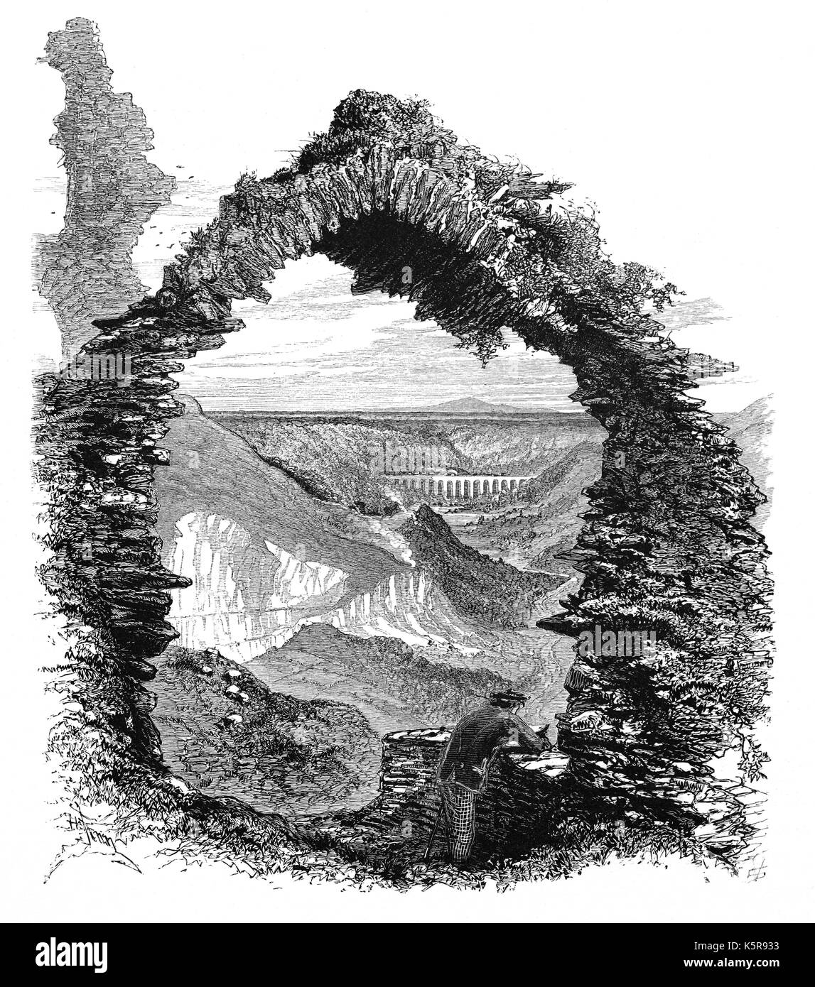1870: The Pontcysyllte Aqueduct that carries the Llangollen Canal across the River Dee, seen through a ruined arch of Castell Dinas Brân. The medieval castle, probably built in 1260,  occupies a prominent hilltop site above the town of Llangollen in Denbighshire, North Wales. Stock Photo