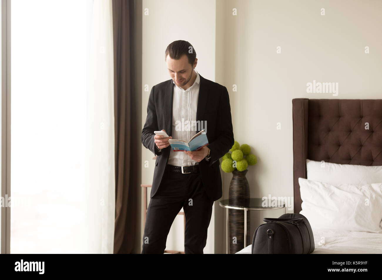 Businessman holds guide brochure and calls taxi or room service. Stock Photo