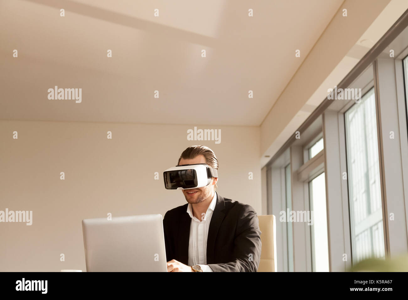 Smiling businessman in vr headset testing application on laptop. Stock Photo
