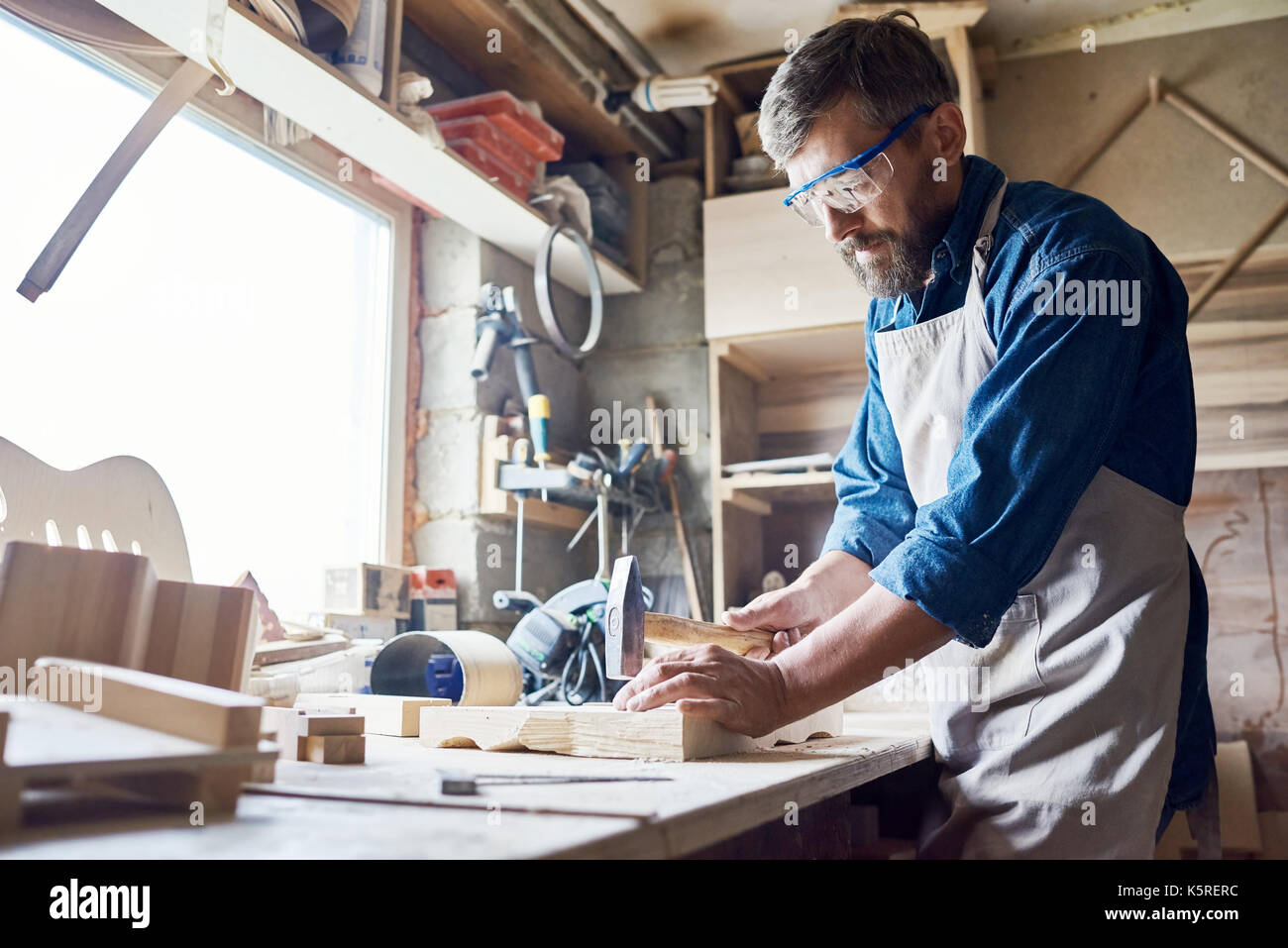 Bearded middleaged craftsman wearing safety goggles and apron Stock