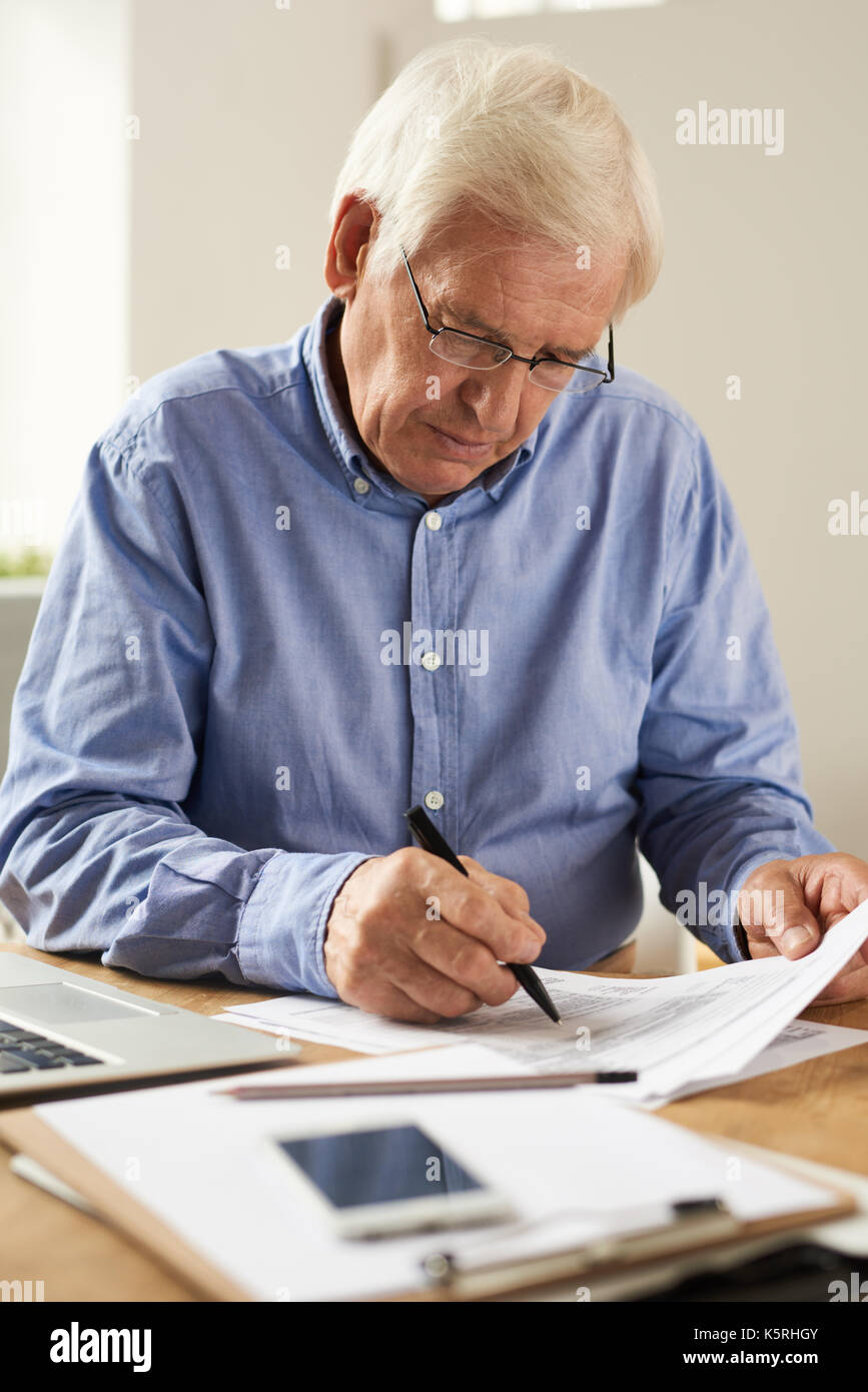 Portrait of modern senior man filling tax report or application form at home sitting at table with laptop Stock Photo