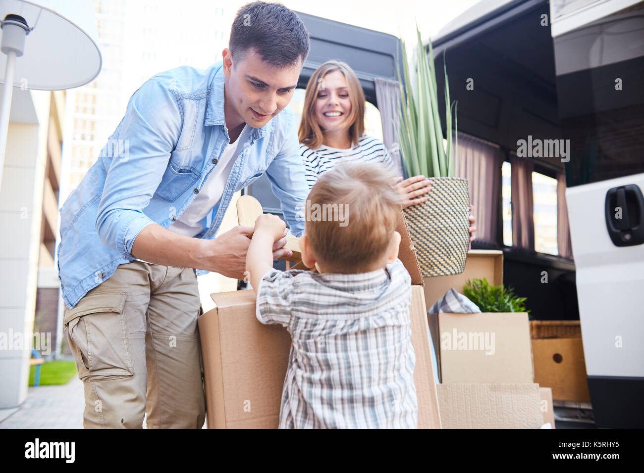 Portrait of happy young family loading boxes to moving van, little boy ...