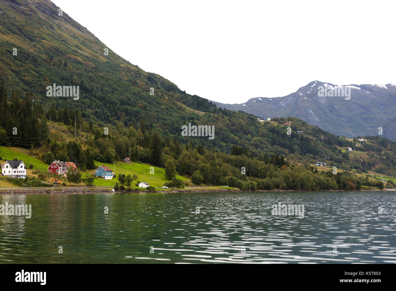norwegian landscape at the foot of a lake with forest background and snowy mountains Stock Photo