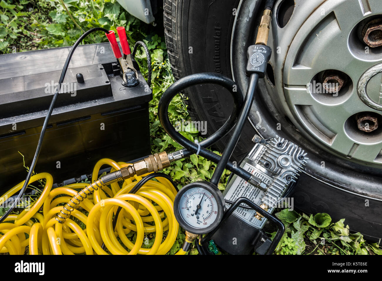 12 volt professional compressor inflator attached to tyre, with brass fittings, coiled air hose and crocodile clips connected to battery. England, UK. Stock Photo