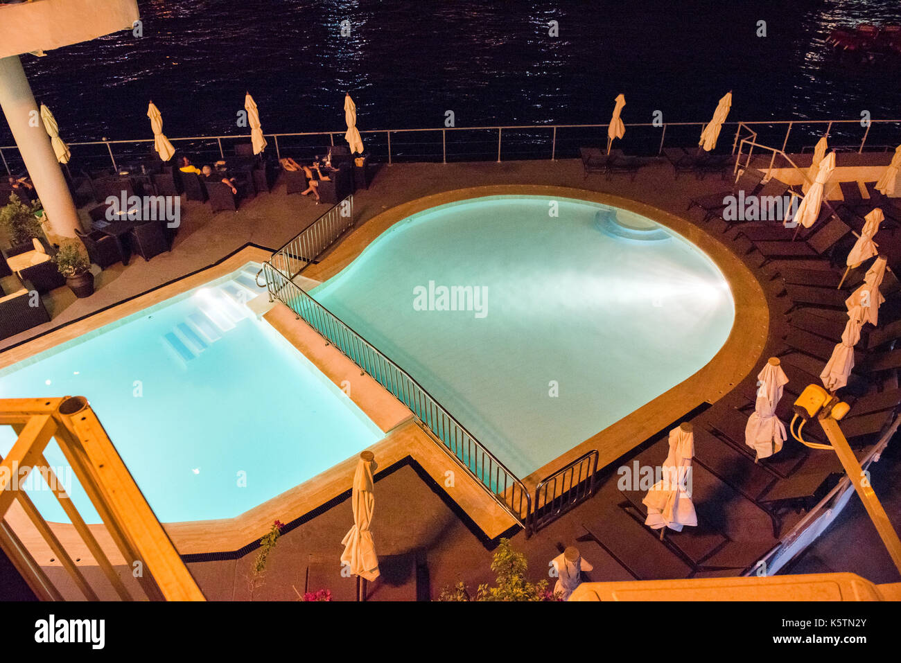 SLIEMA, MALTA - AUGUST 22, 2017: Tourists relaxing near a sea luxurios swimming pool at night with a great panoramic night cityscape to Valletta Stock Photo