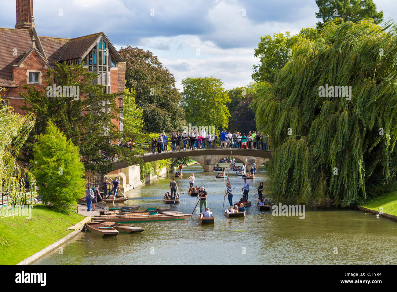 Tourists crossing a bridge over River Cam with punters underneath and the Jerwood Library on the left, Cambridge, UK Stock Photo