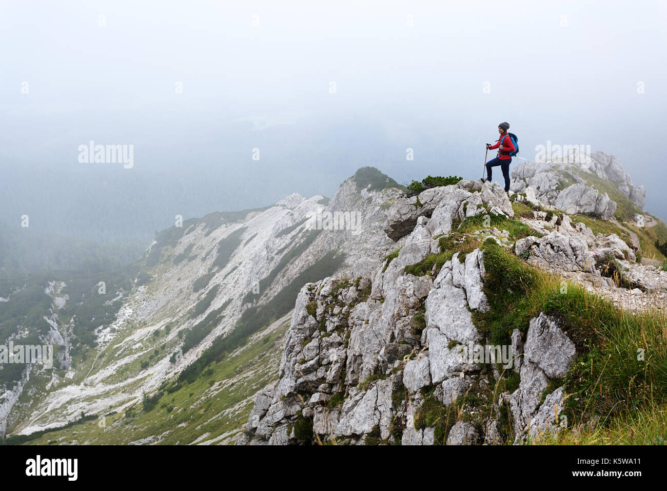Woman in red windproof jacket standing on top of the mountain covered in fog, Visevnik, Julian Alps, Slovenia. Stock Photo