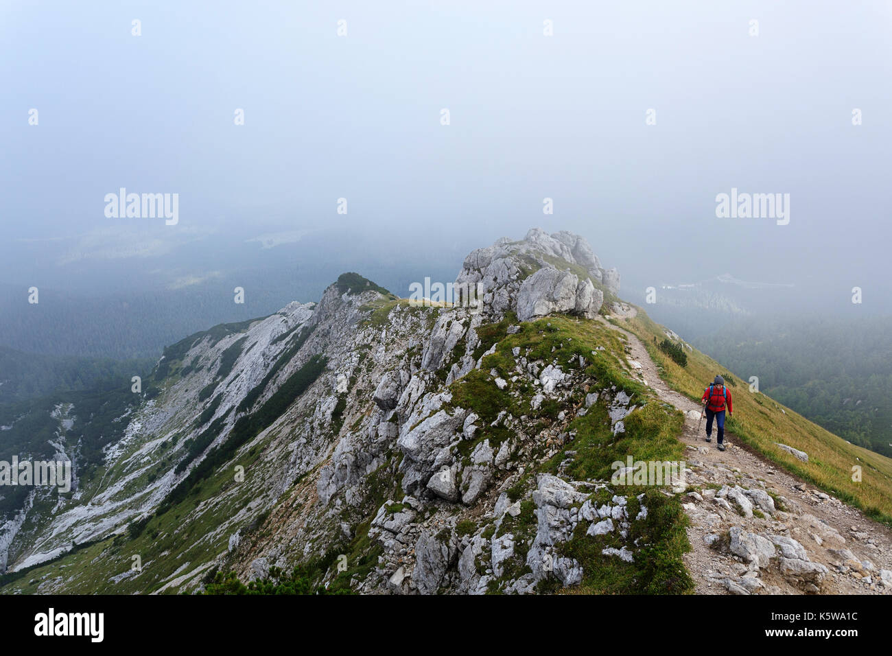 Woman in red windproof jacket hiking on a mountain covered in fog, Visevnik, Julian Alps, Slovenia. Stock Photo
