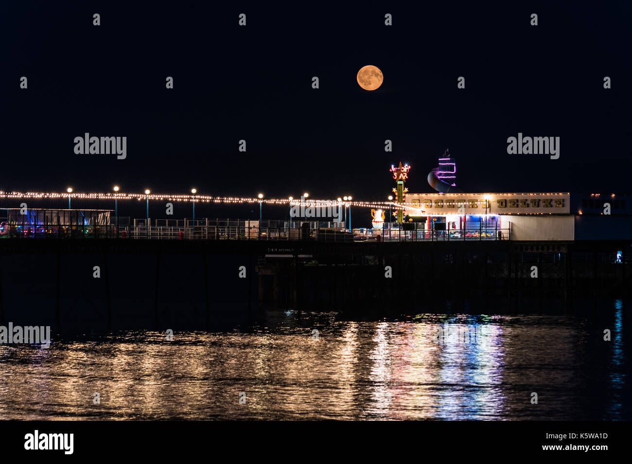 Rising full moon over illuminated pier Stock Photo