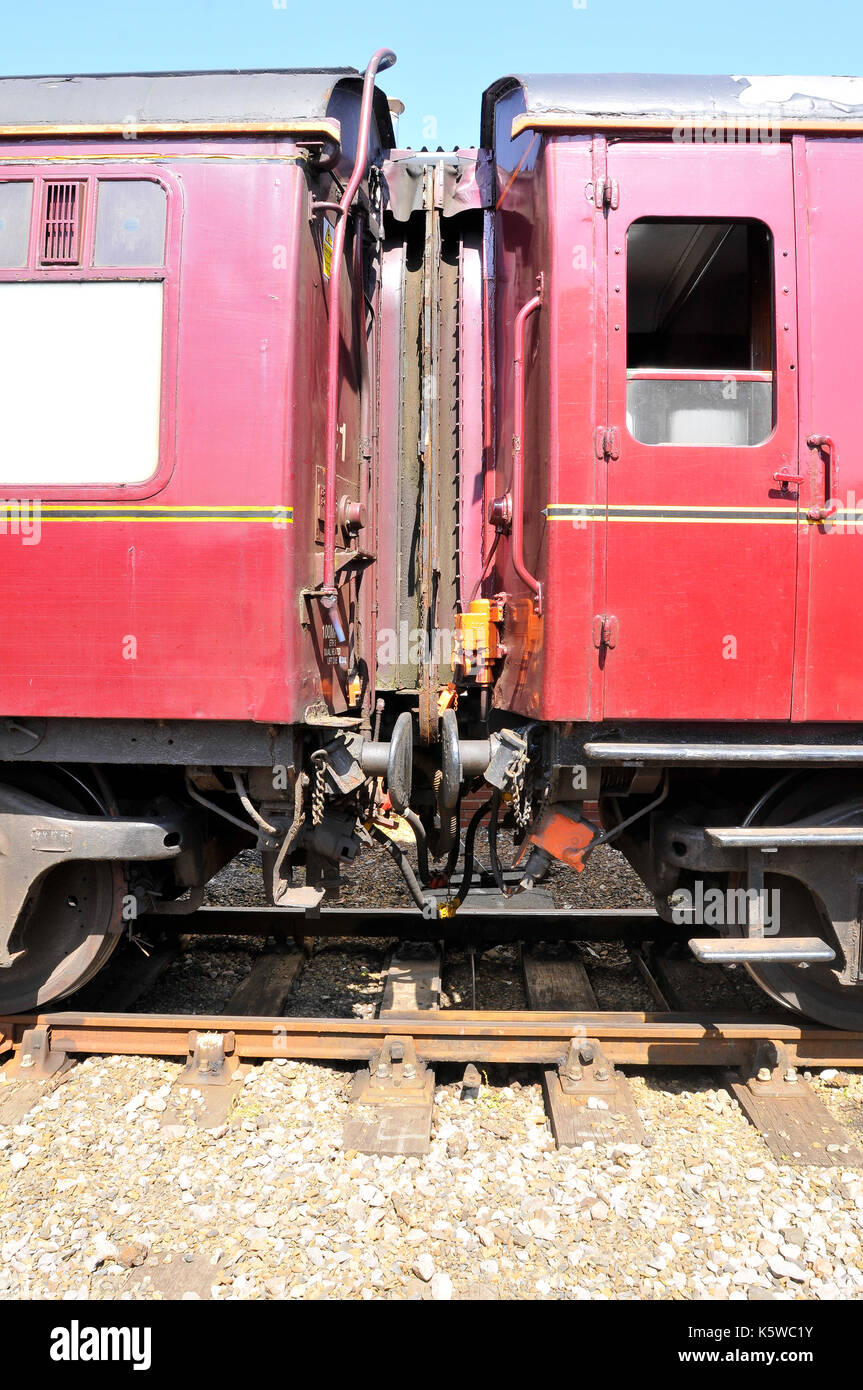 two railway carriages end to end connected by couplers and buffers on the rails and tracks coupled up for passenger services to walk through between Stock Photo