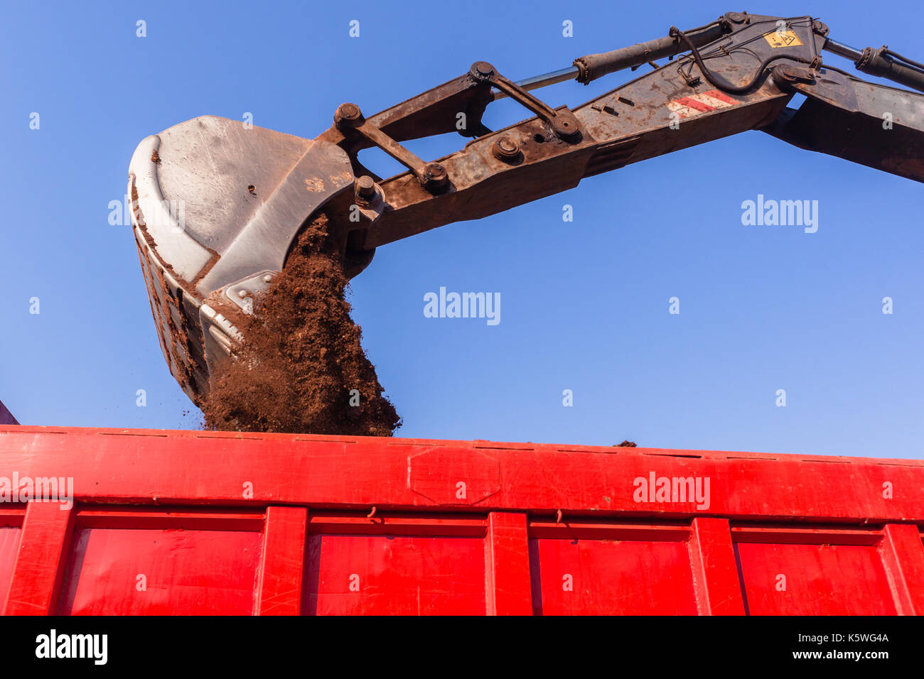Excavator earthworks machine loading soil into truck bin closeup