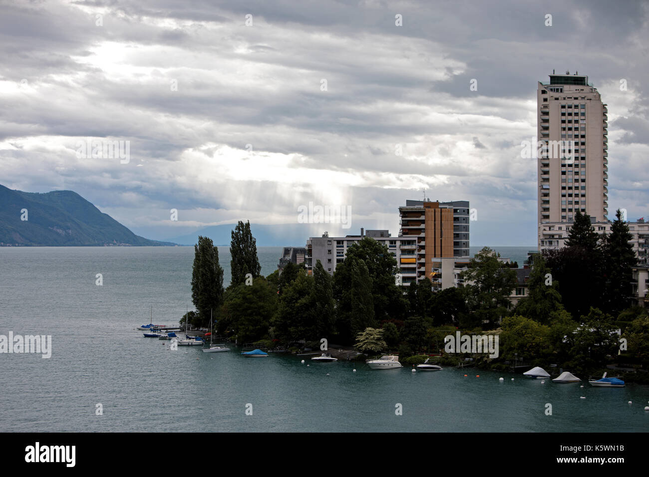 High rise apartment blocks in the center or Montreux on Lake Geneva in Switzerland. Boats and small yachts are moored up alongside the promenade with  Stock Photo
