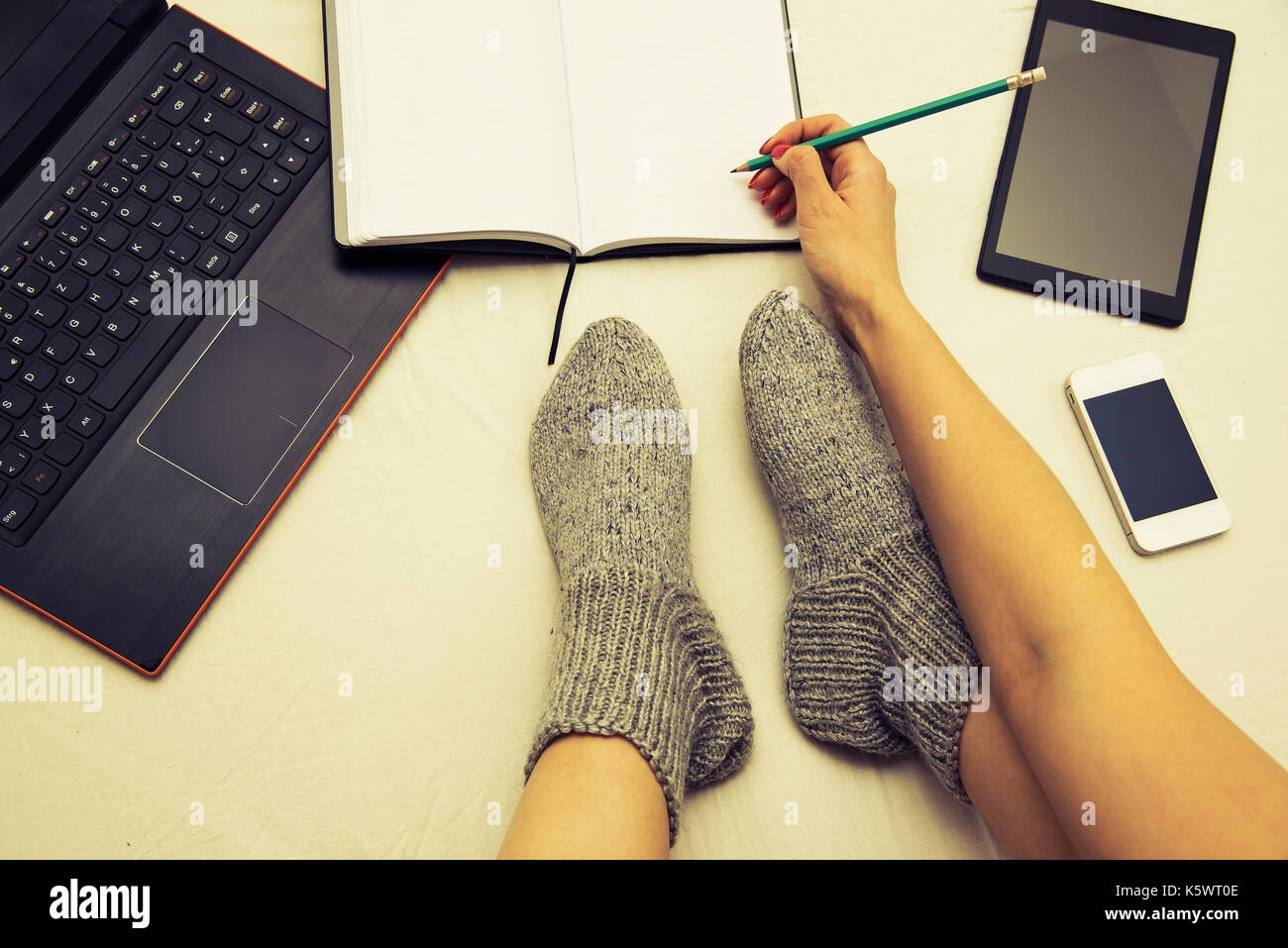 female legs wearing surrounded by multiple communication devices writing in a notebook Stock Photo