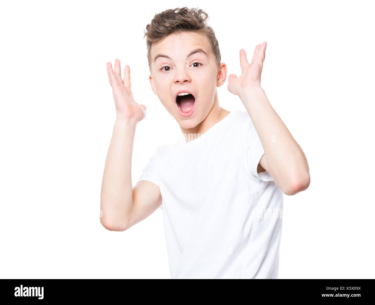 Emotional portrait of amazed or surprised teen boy in white t-shirt. Funny cute cheerful child screaming with wide open mouth, isolated on white backg Stock Photo