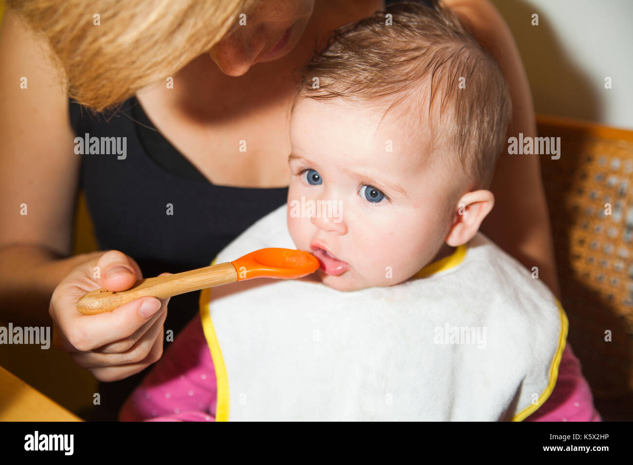 Mother feeding a 6-month old baby with a spoon for the first time Stock Photo