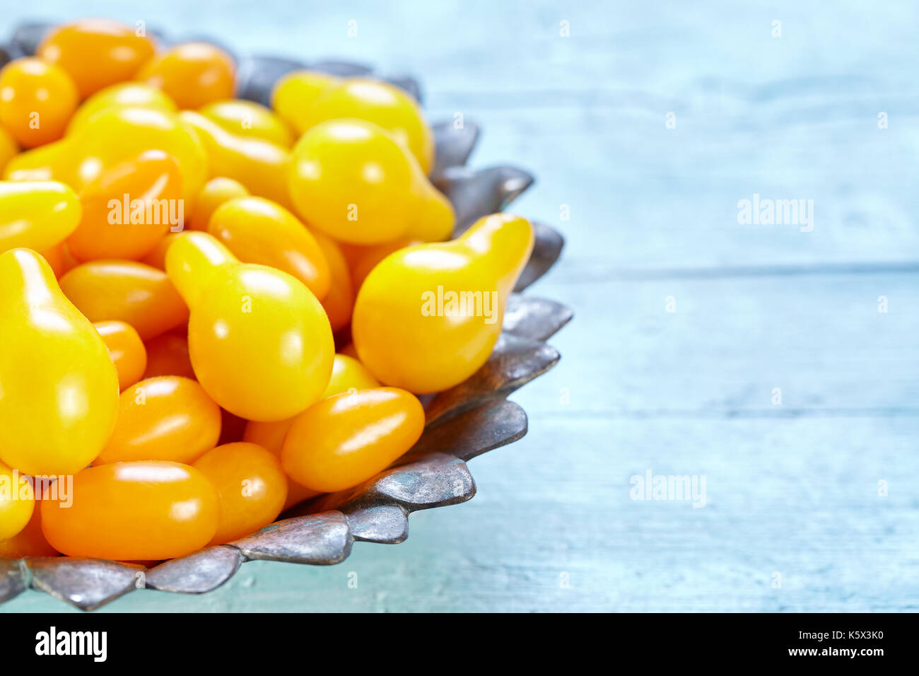 Bowl with mix of yellow pear and datterino heirloom cherry tomatoes on light blue wooden background, photo with copy space. Stock Photo