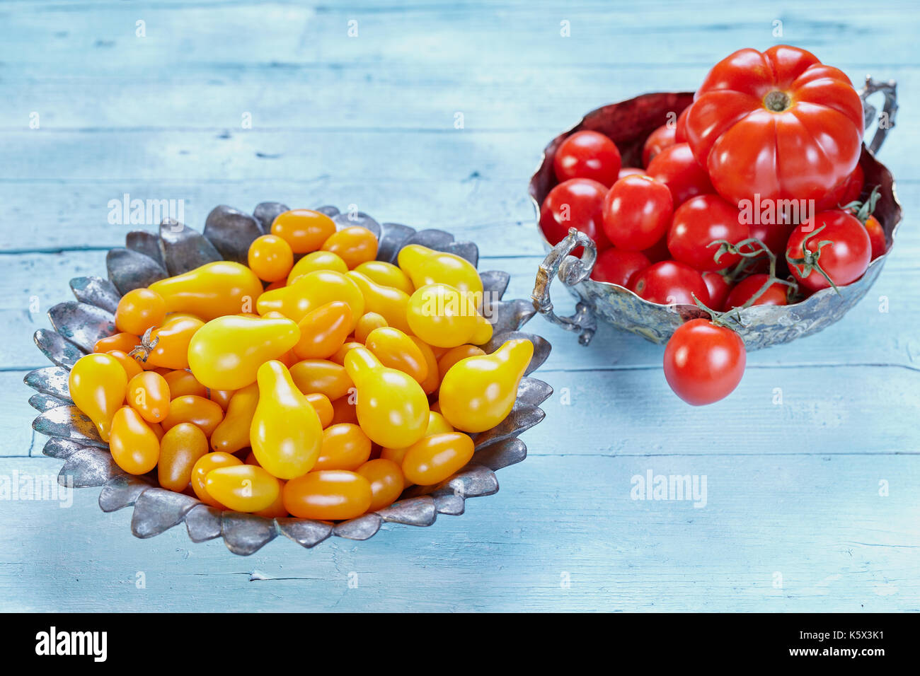 Varieties of tomatoes: yellow pear cherry, plum or datterino cherry, red cherry and beefstick tomato, on light blue wooden background. Stock Photo