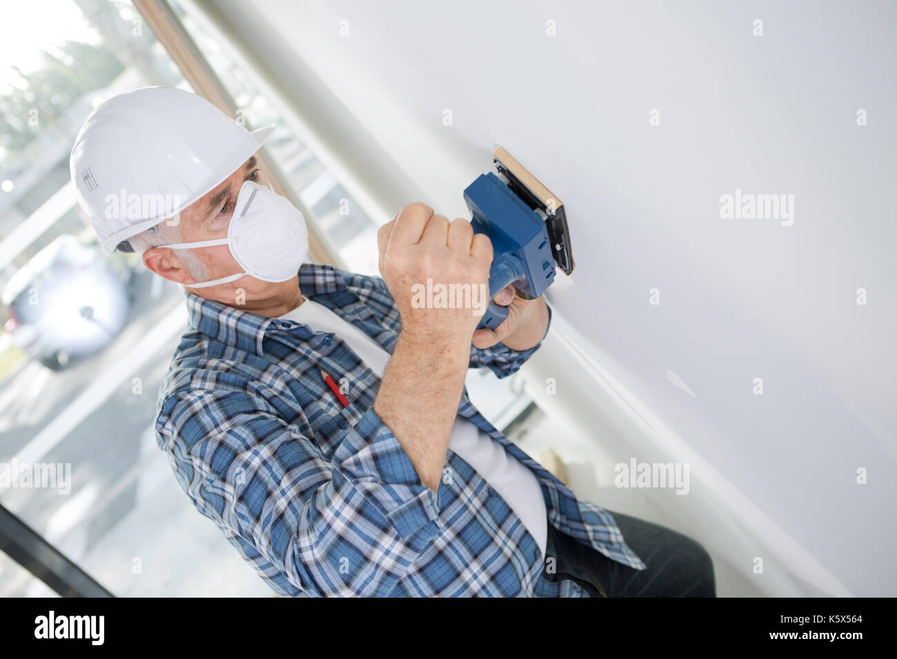 aged builder in hardhat sanding wall indoors Stock Photo