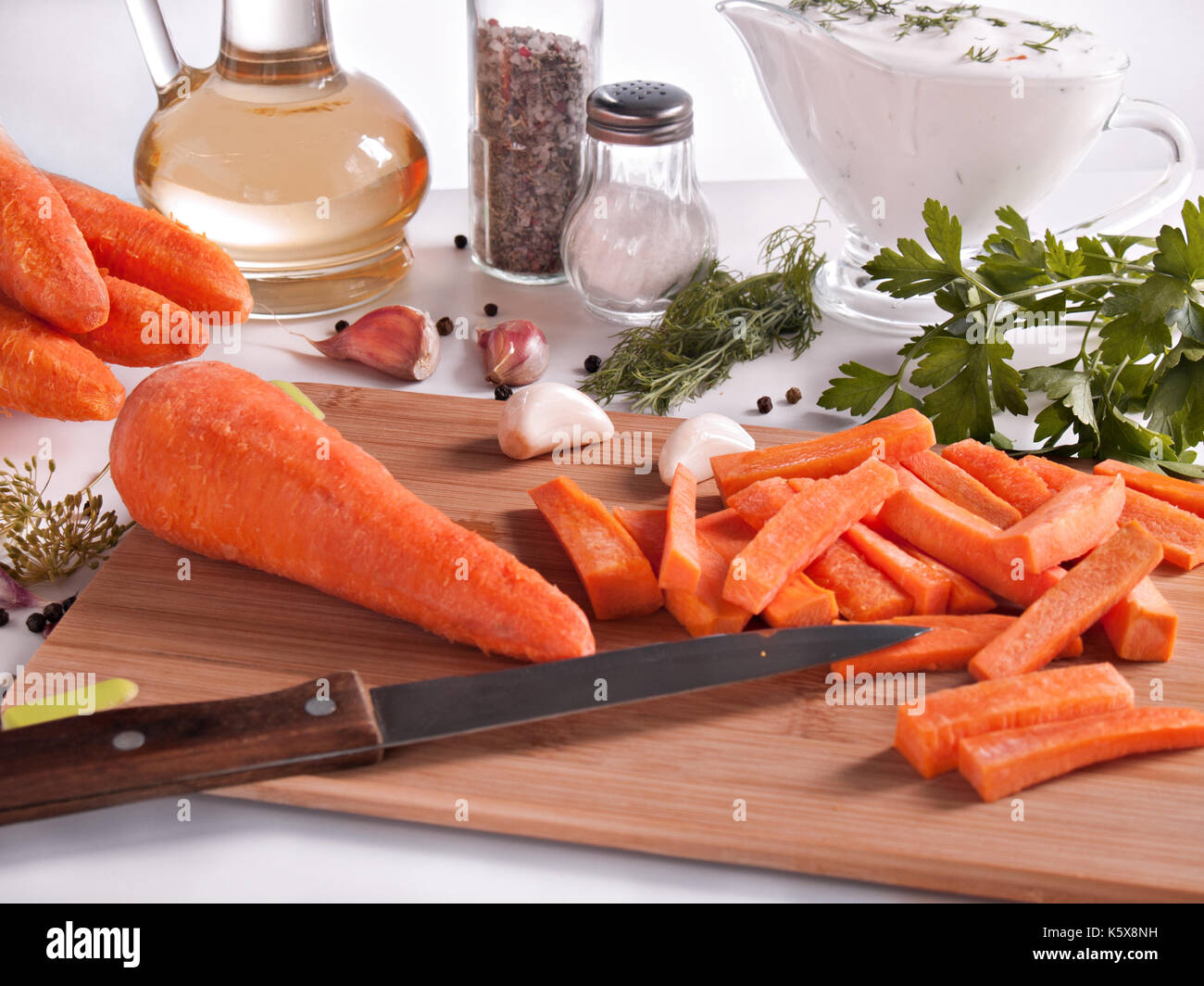 Carrots chopped on chopsticks surrounded by greenery, parsley, dill, garlic, pepper, vegetable oil in a bottle with a stopper, pepper and salt in jars Stock Photo