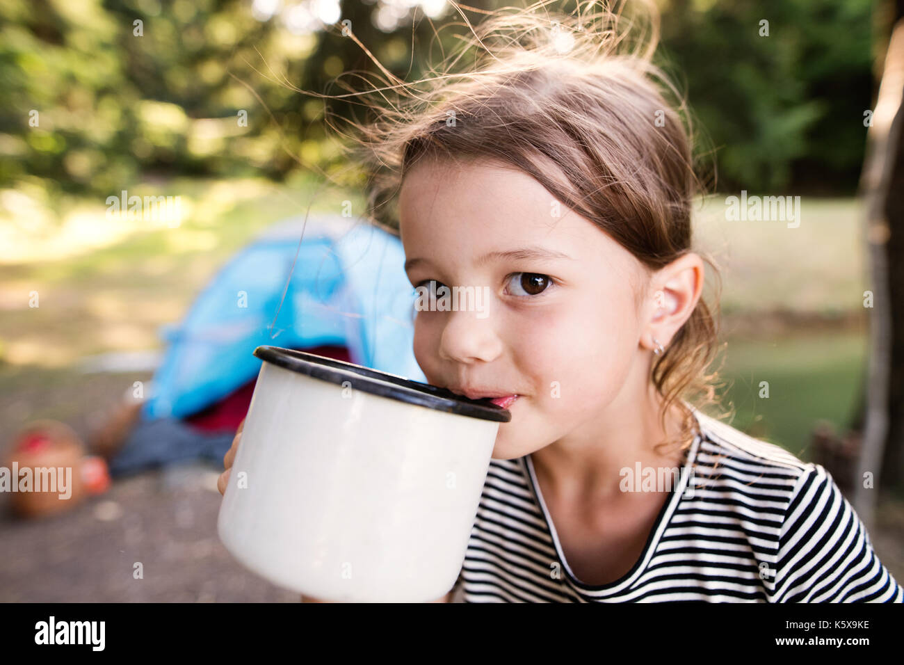 Cute little girl camping outdoors, drinking water. Stock Photo