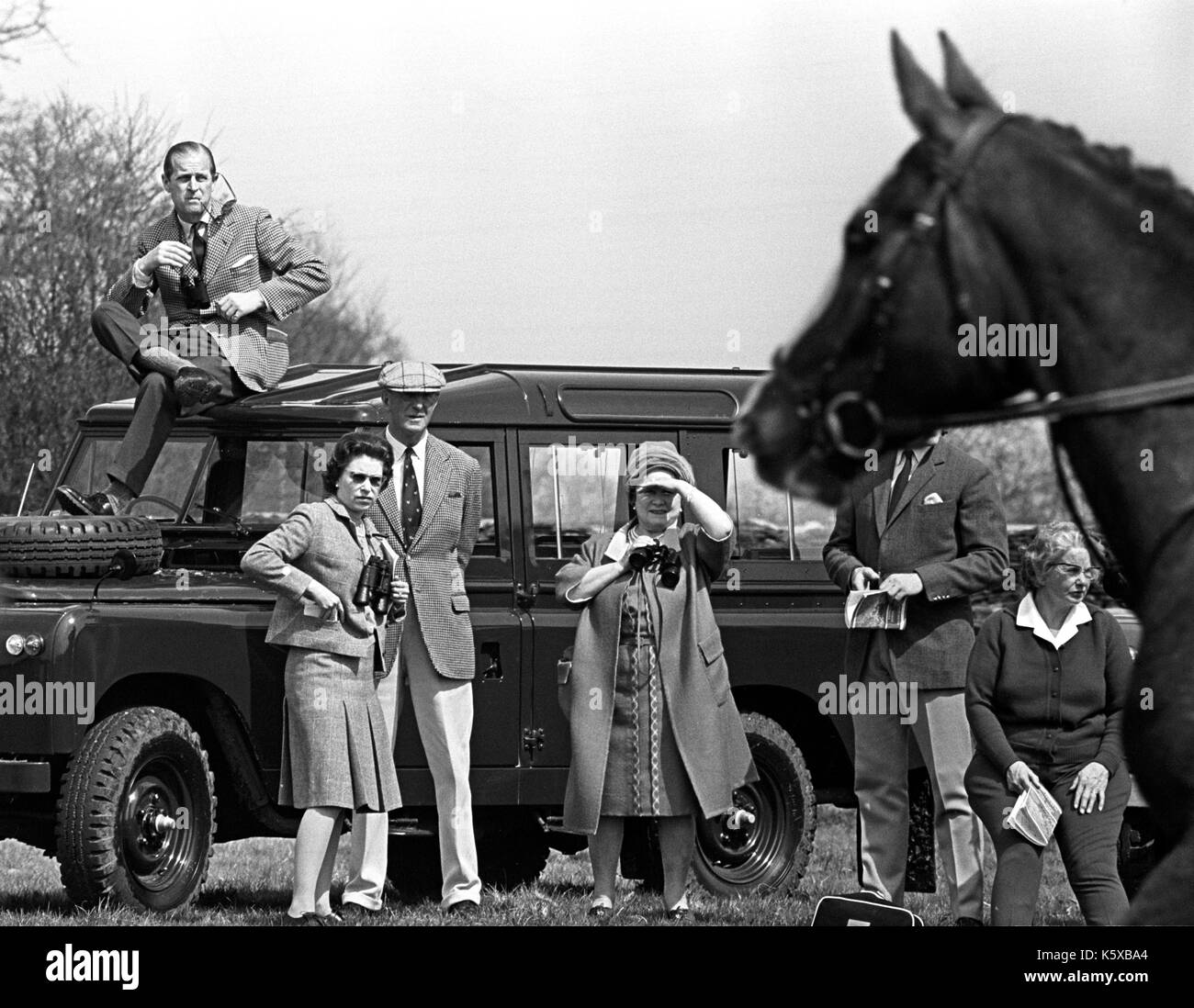 Prince Philip, the Duke of Edinburgh, perches on the roof of a Land Rover but Queen Elizabeth II (l, with dark glasses), the Queen Mother and Duke of Beaufort prefer a ground-level view of competitors during the Horse Trials at Badminton, Gloucestershire. Stock Photo