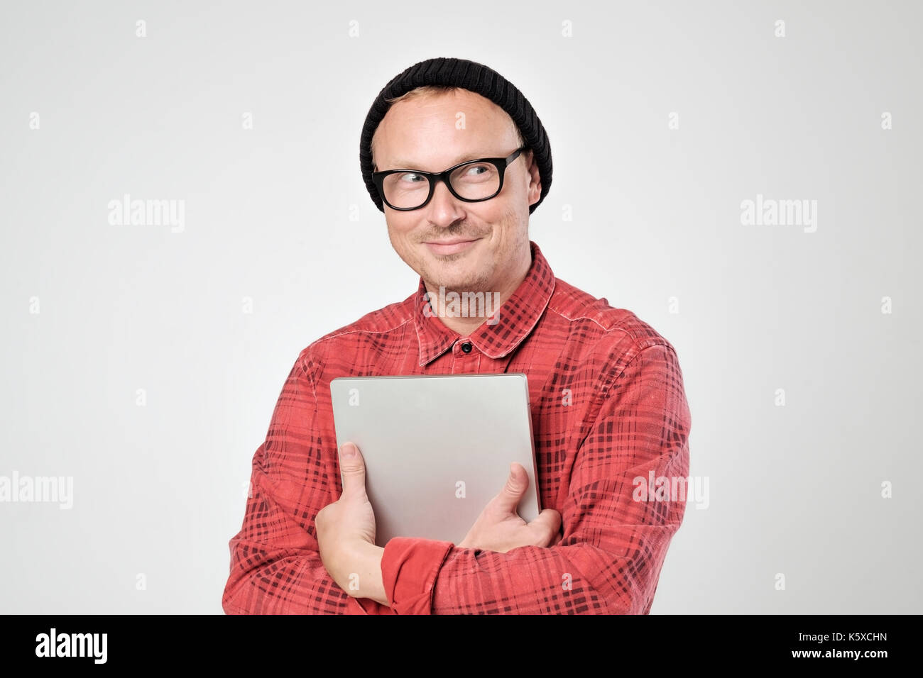 A young programmer in a black hat is holding a laptop in his han Stock Photo