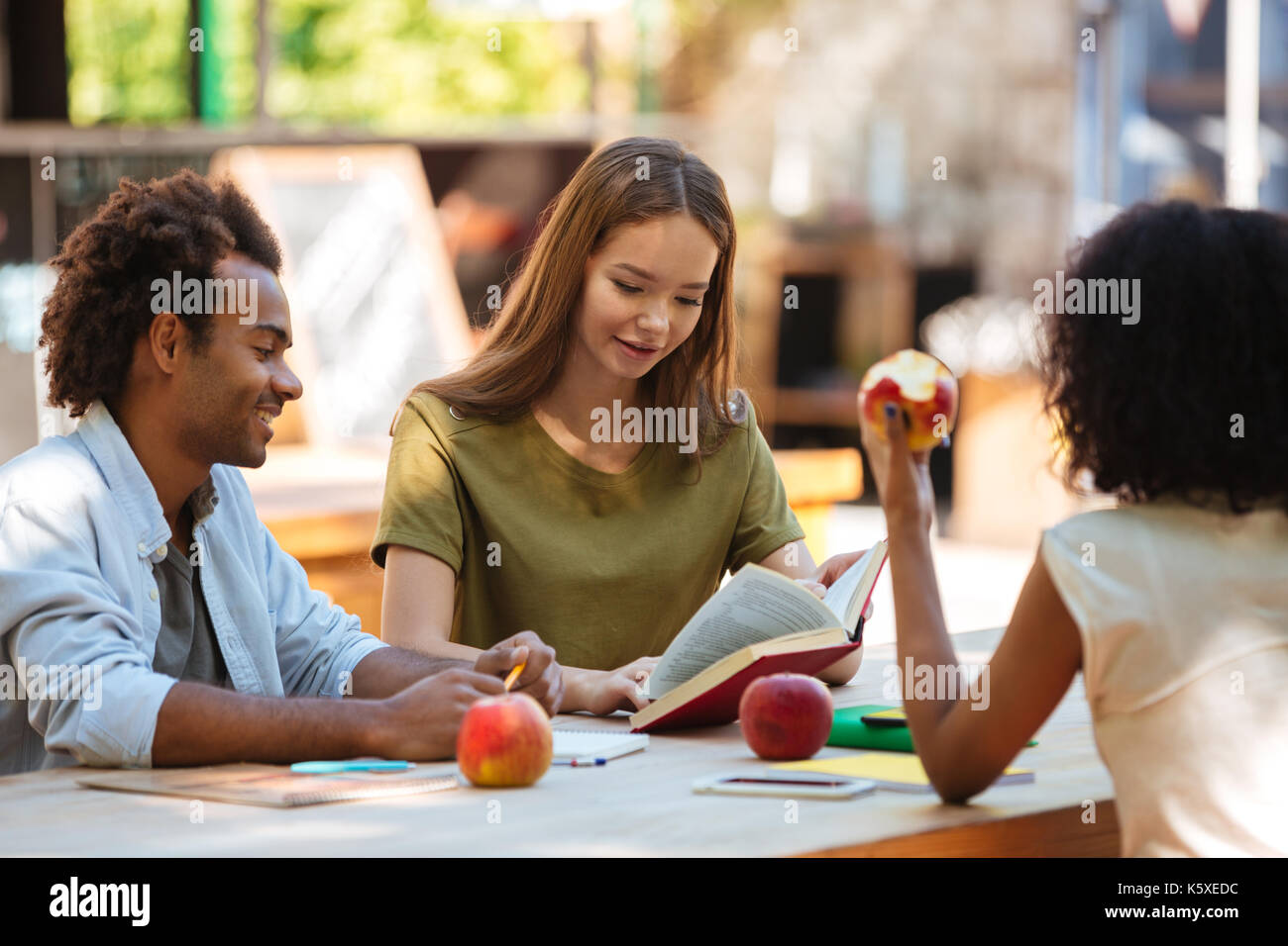 Happy three friends sitting by the table outdoors Stock Photo