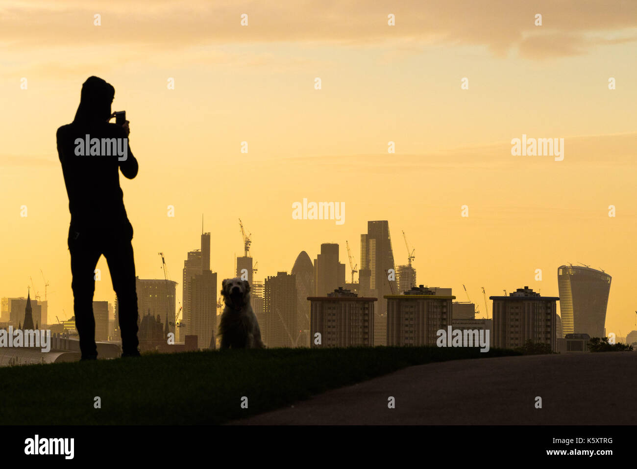 London, UK. 11th Sep, 2017. London, September 11 2017. An early morning dog walker uses his smartphone to capture the London skyline as a new day breaks over the city. Credit: Paul Davey/Alamy Live News Stock Photo
