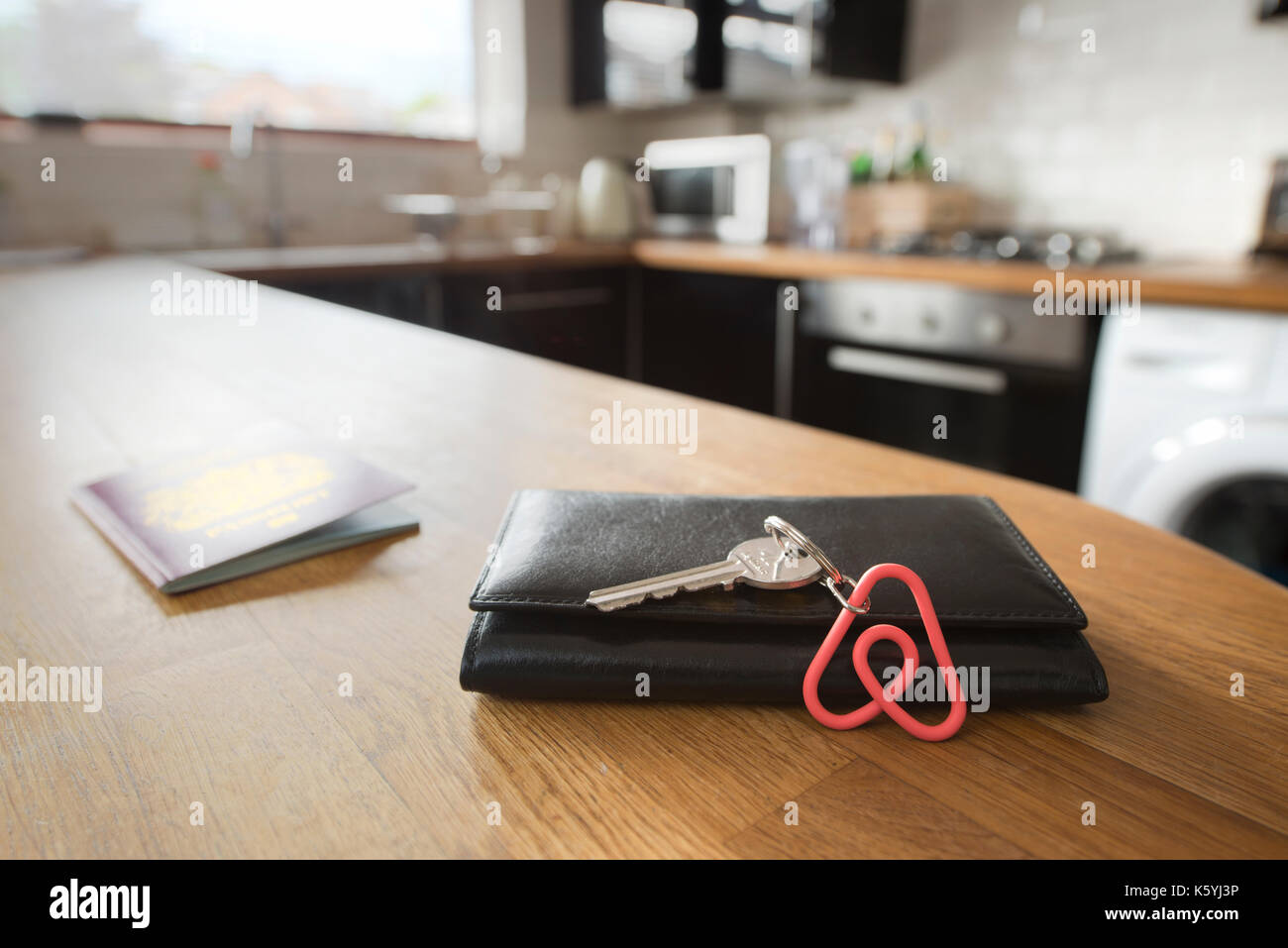 An Airbnb keyring rests against a wallet in the kitchen of an Airbnb apartment available to hire by guests, with a British passport behind. Stock Photo
