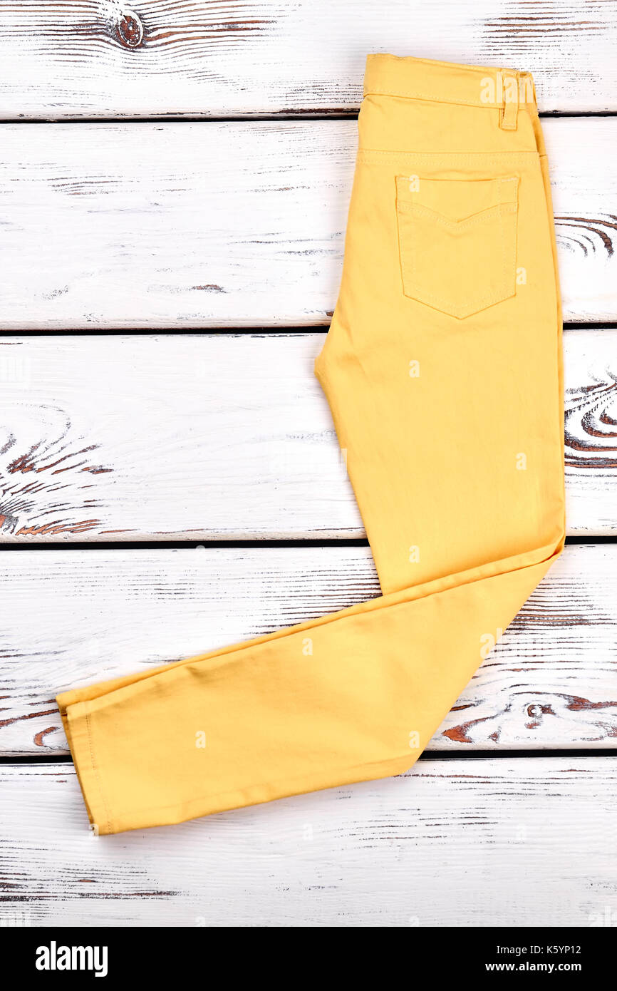Girls new yellow trousers. Young lady yellow color pockets pants folded on  white wooden background. Woman fashion clothes store Stock Photo - Alamy