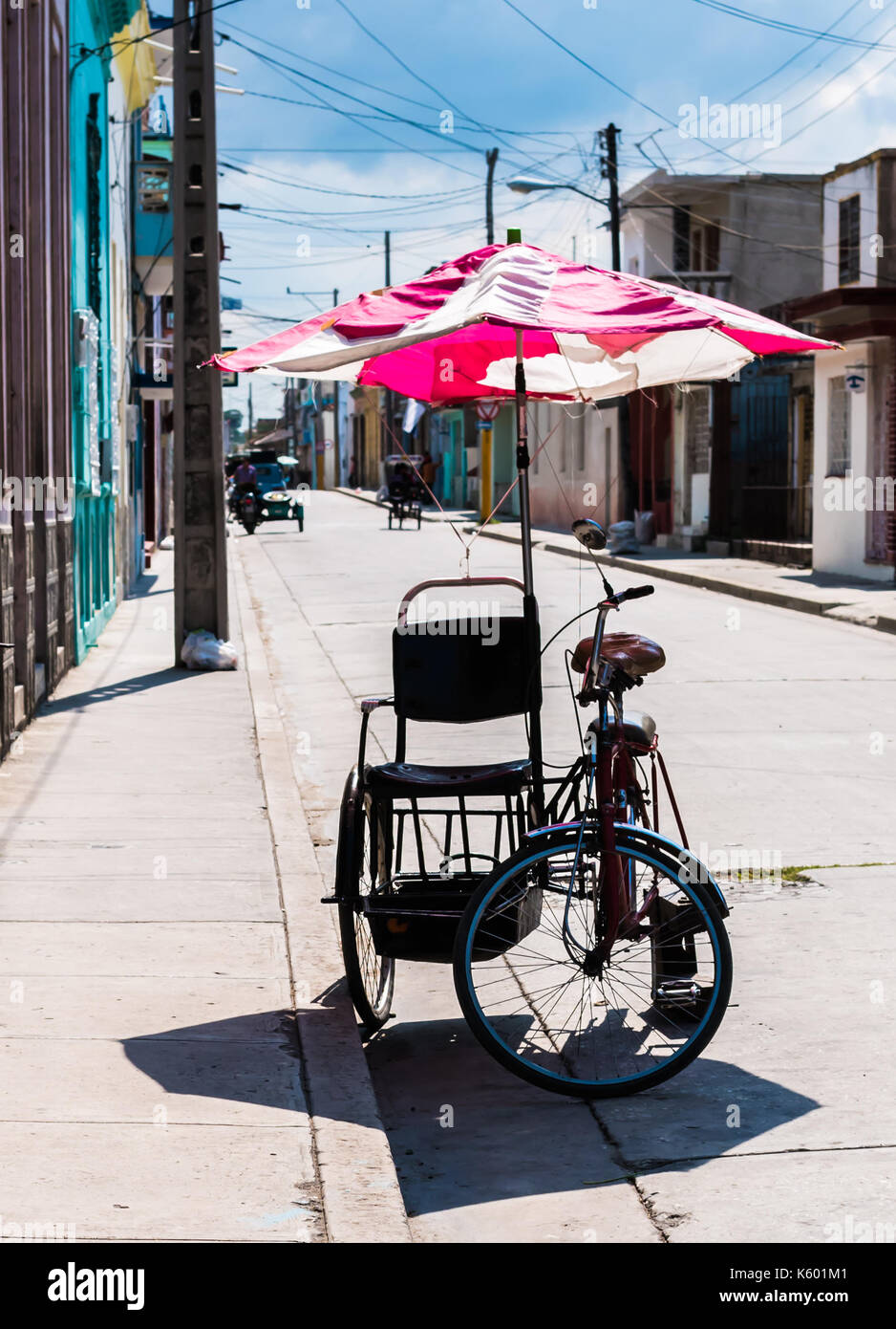 Bicycle taxi, pedicab bike parked on the side of a street. Colorful umbrella attached to the cart to provide shade for riders. Stock Photo
