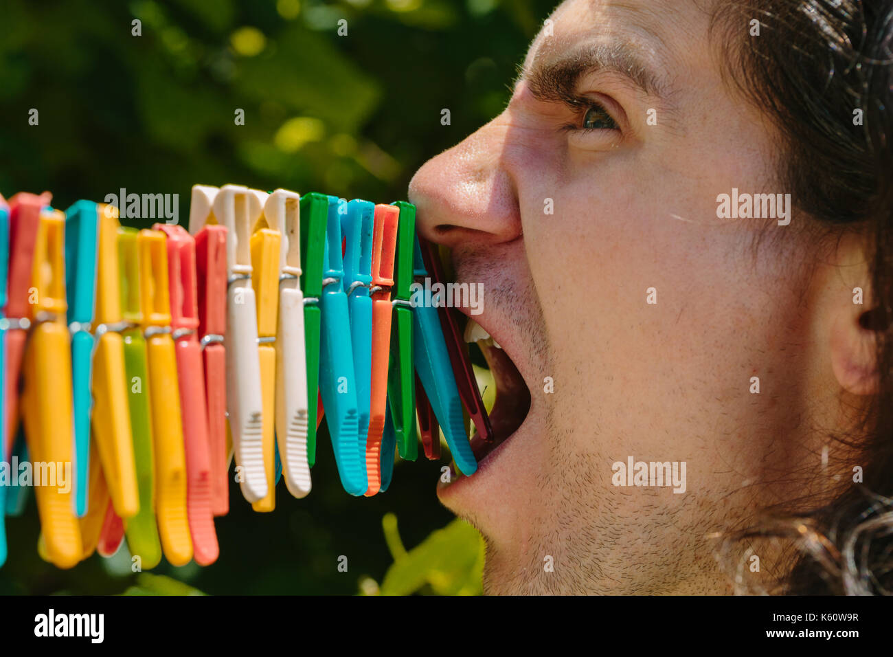 Man tries to bite off clothes pegs. Stock Photo