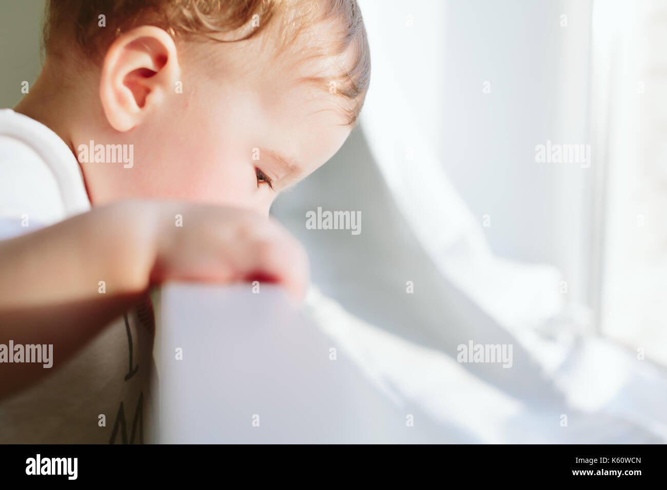 Little baby holds onto the bed and looks somewhere. Stock Photo