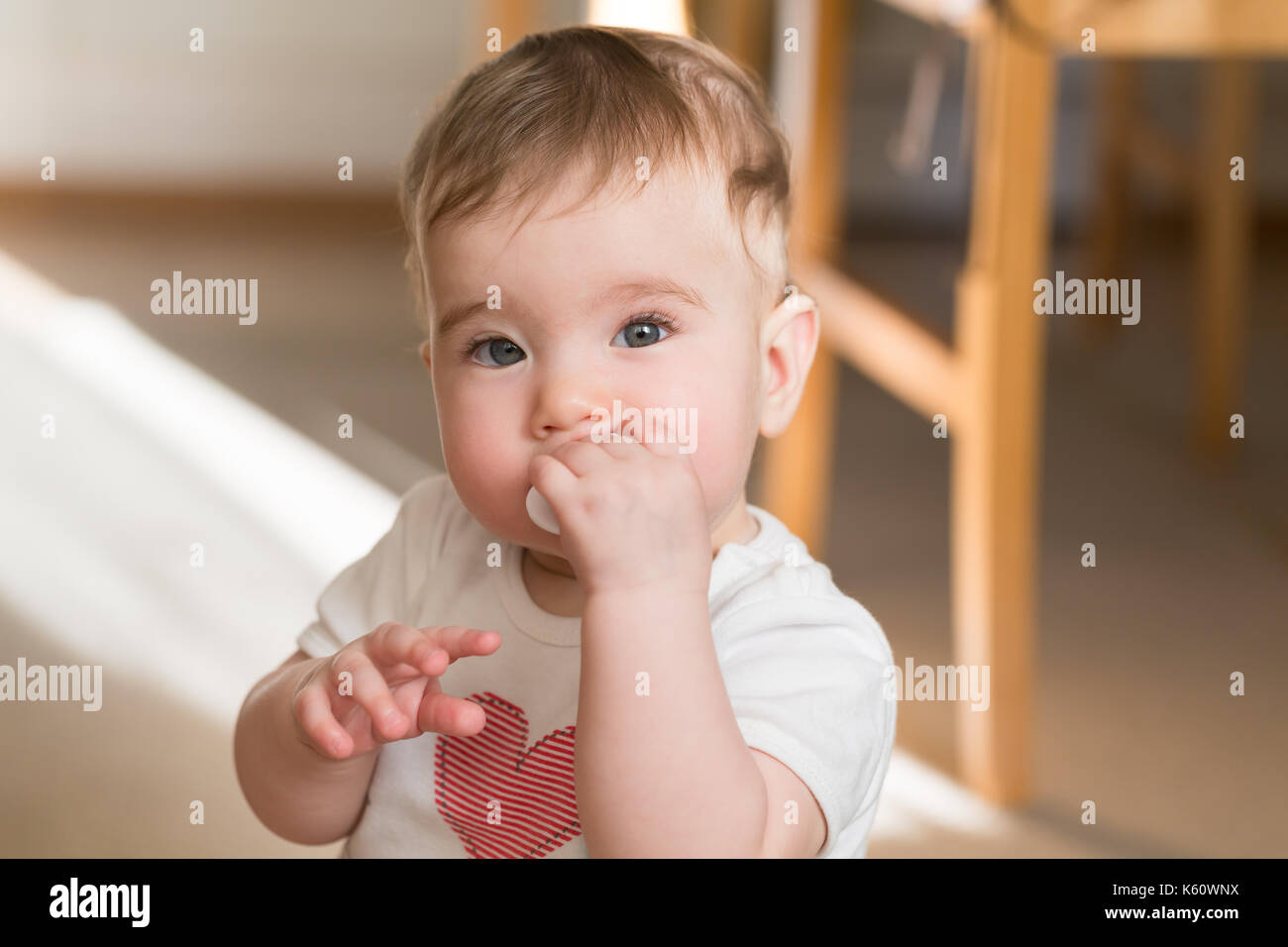 Beautiful little baby with hand near mouth. Close up portrait in home. Stock Photo