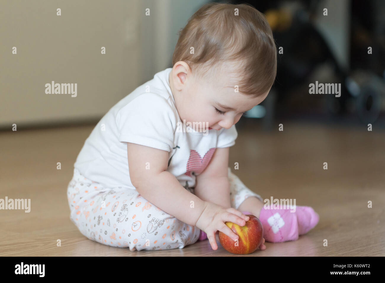 Little child sitting at home on the floor with a red apple. Stock Photo