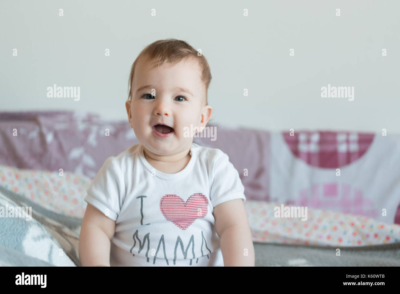 Little smiling child is sitting on the bed at home. Stock Photo