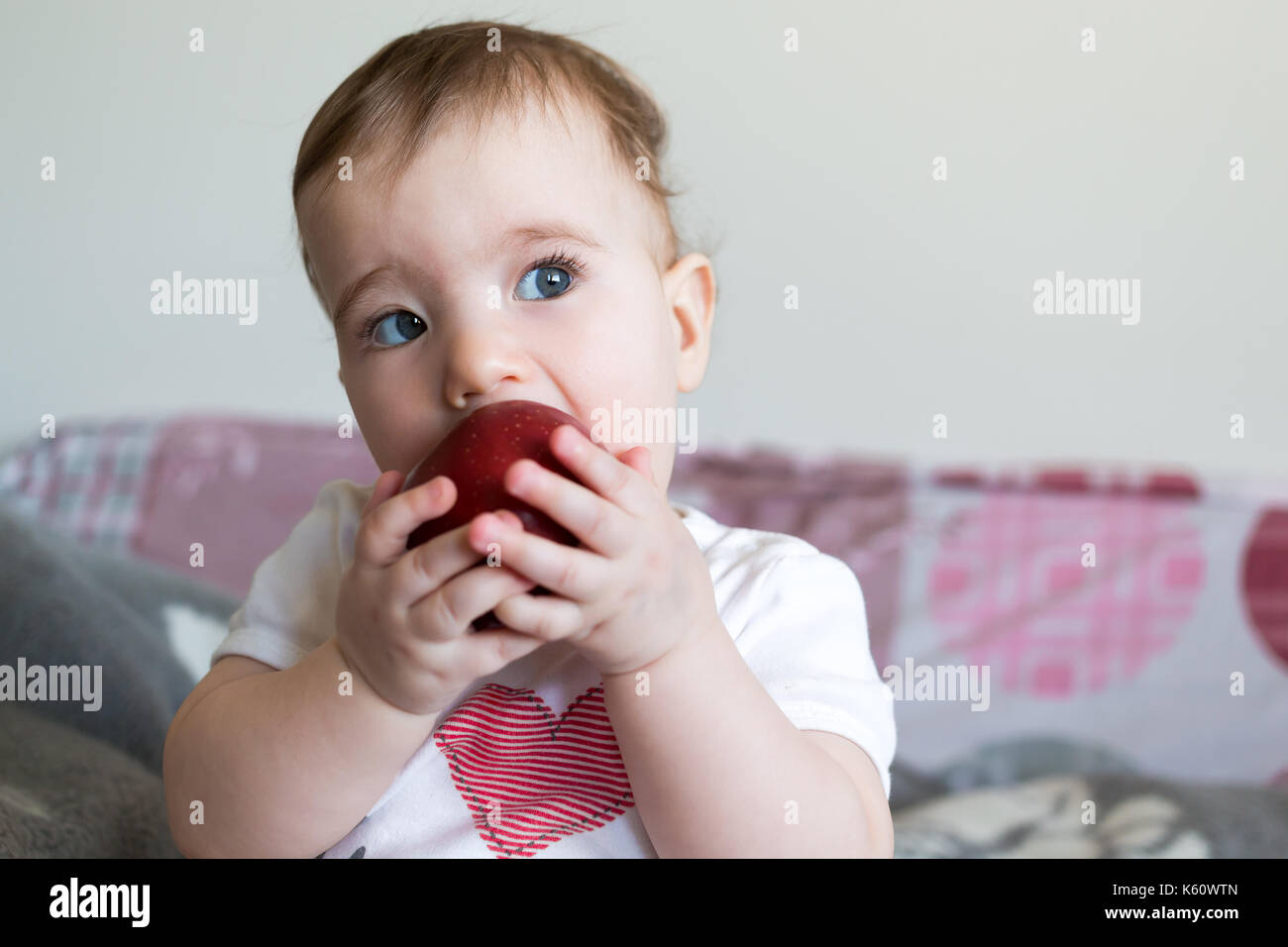 Small child eats a red apple at home closeup. Stock Photo